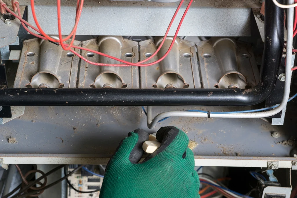 HVAC technician performing furnace capacitor maintenance inside a heating system